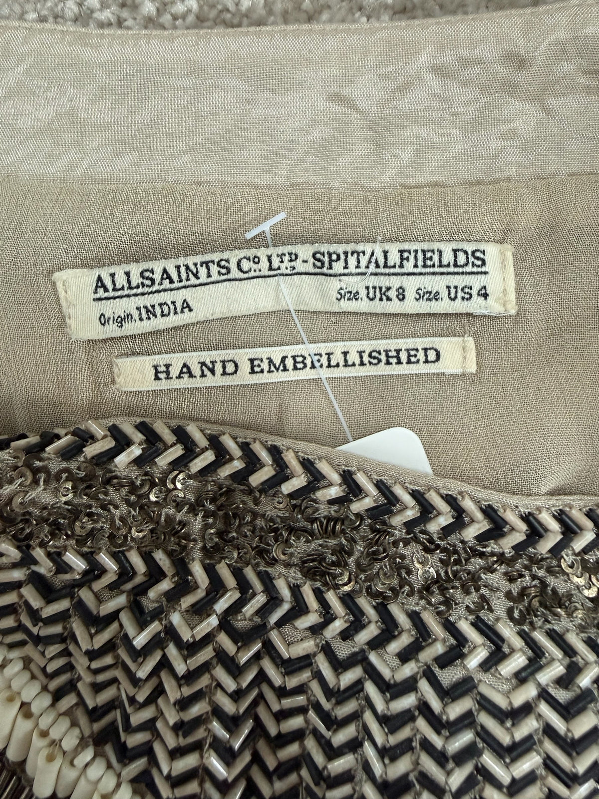 Style Reset AllSaints Spitalfields mini skirt label showing hand-embellished beadwork in black, cream, and bronze.