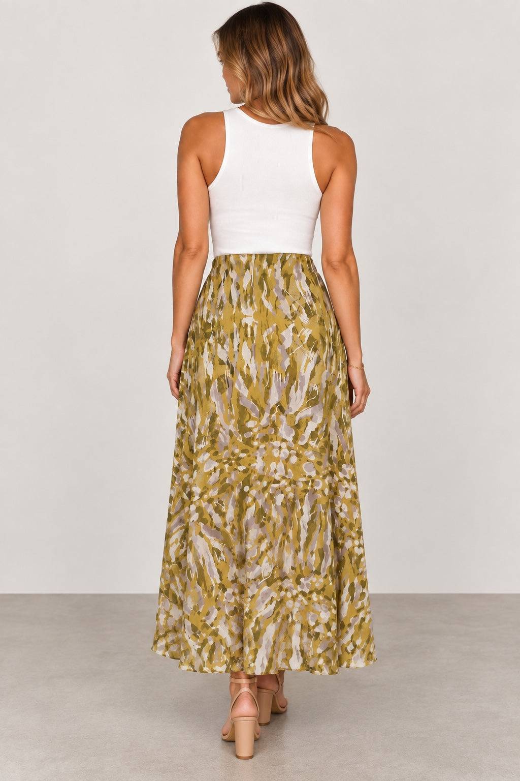 Style Reset model wearing an ALLSAINTS olive, mustard, and grey abstract print high-low maxi skirt with a white tank
