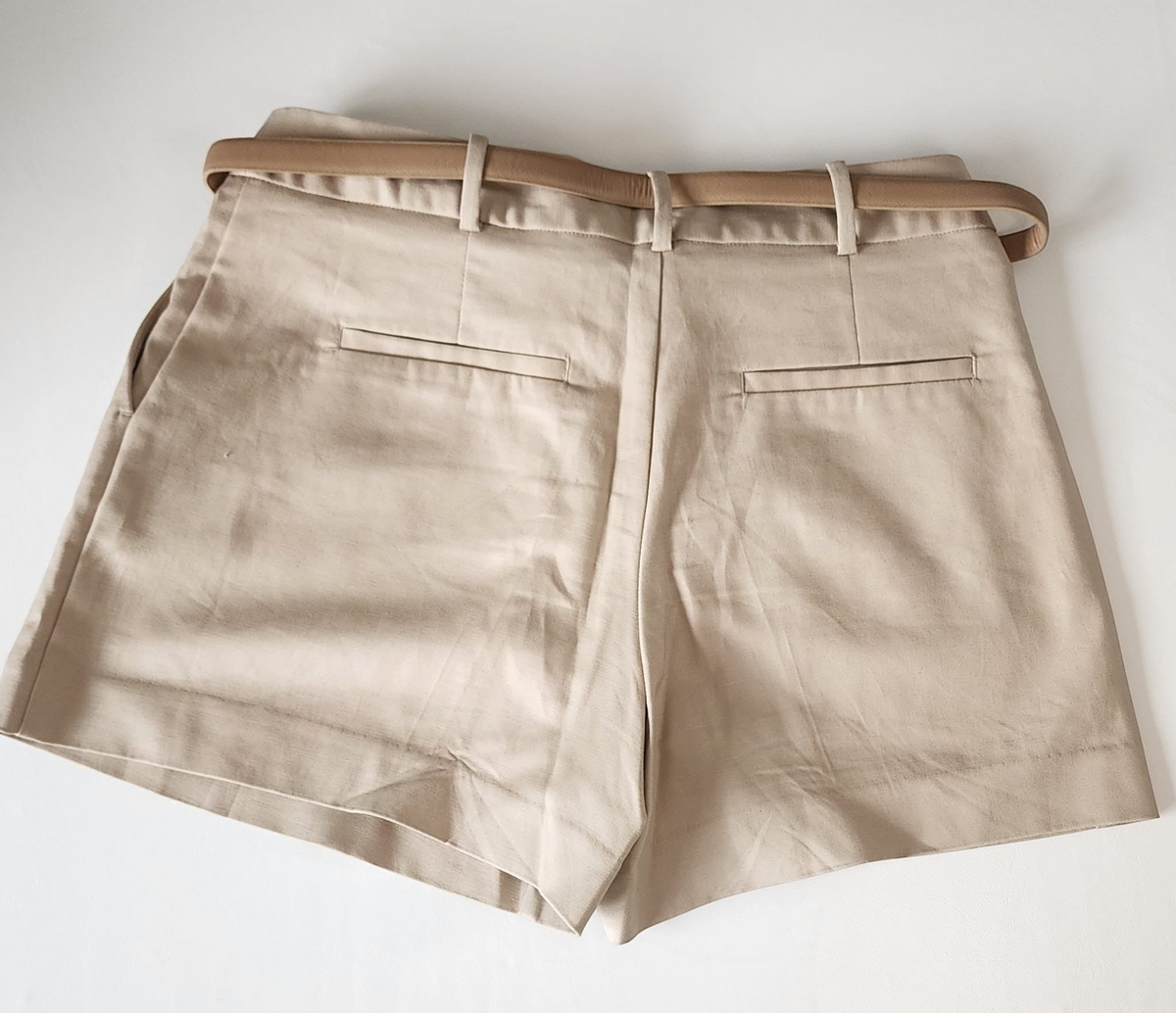 Style Reset beige high-waisted tailored shorts with a slim belt and faux back pockets, shown from the rear view.