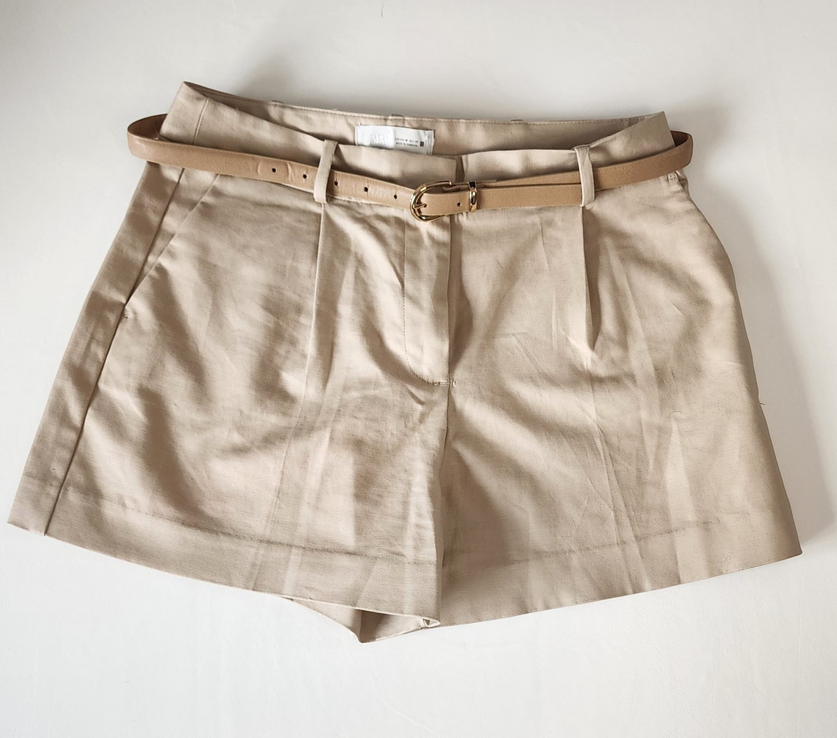Style Reset beige high-waisted tailored shorts with front pleats and a matching slim belt featuring a gold-tone buckle.