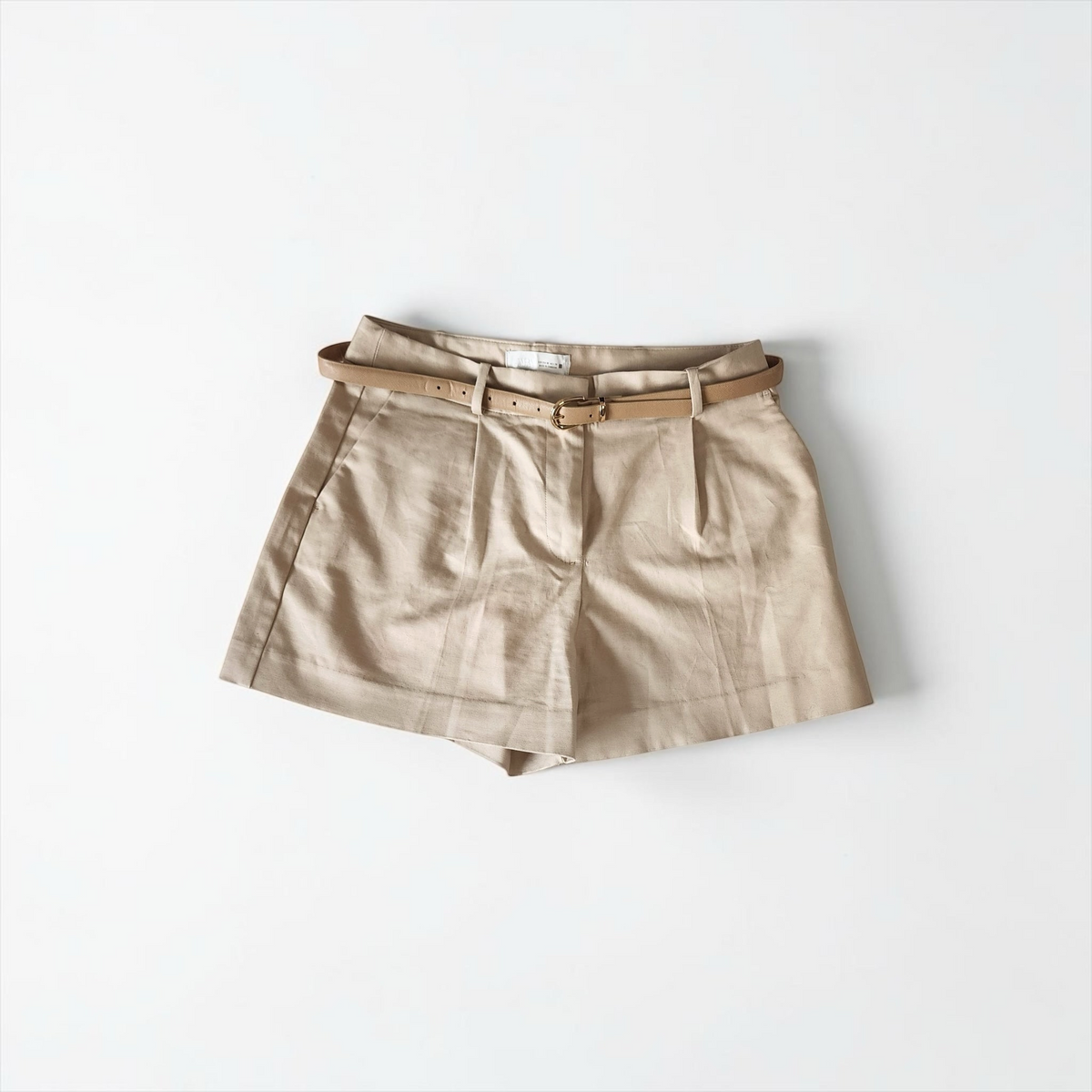 Style Reset beige high-waisted tailored shorts with front pleats and a matching slim belt with a gold-tone buckle.
