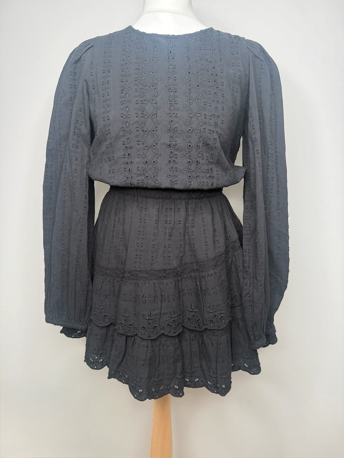 Style Reset black long sleeve mini dress in broderie anglaise fabric with a tiered skirt and scalloped hem detail.