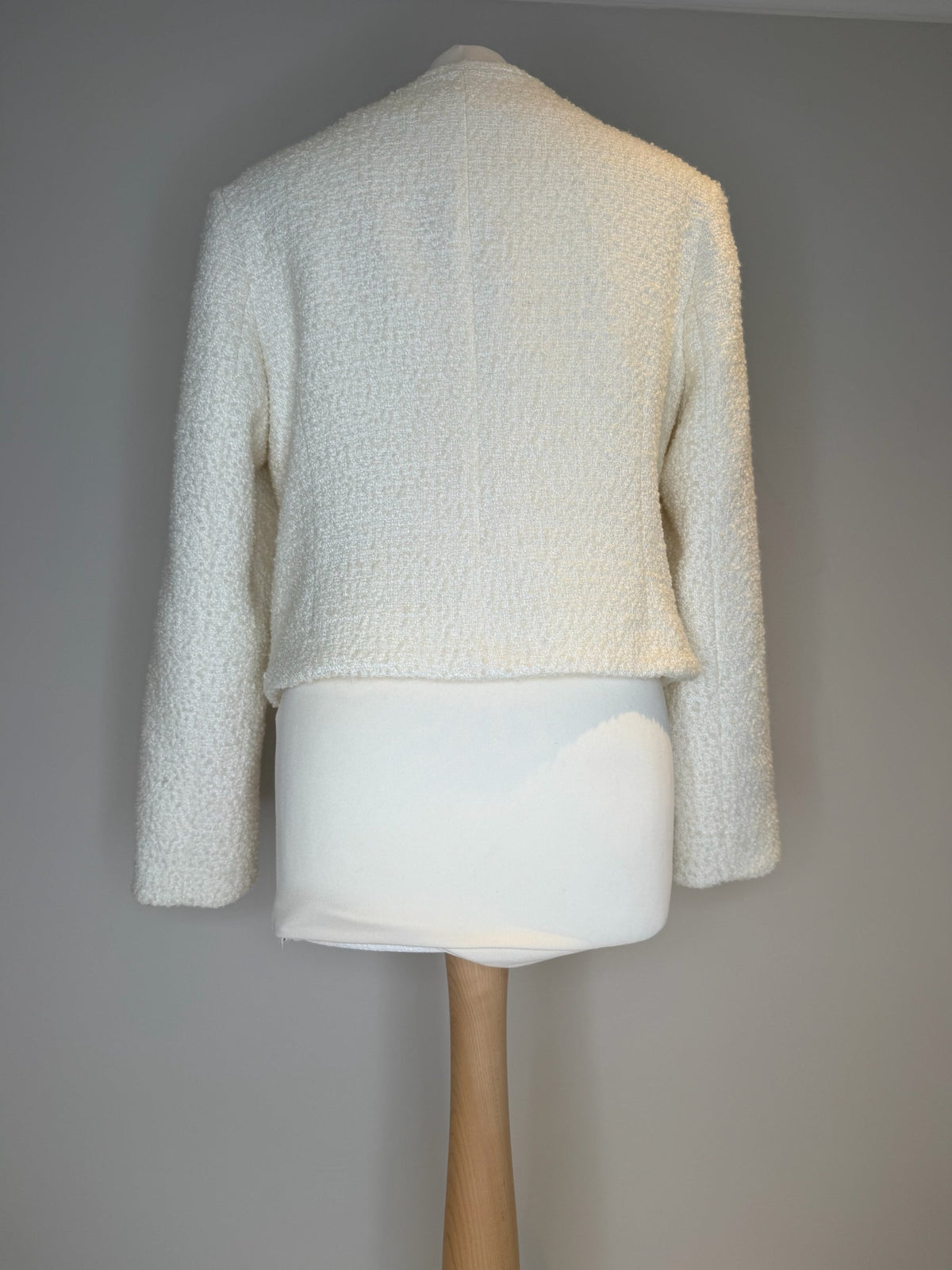 Style Reset cream boucle textured jacket viewed from the back on a mannequin, featuring a collarless design.