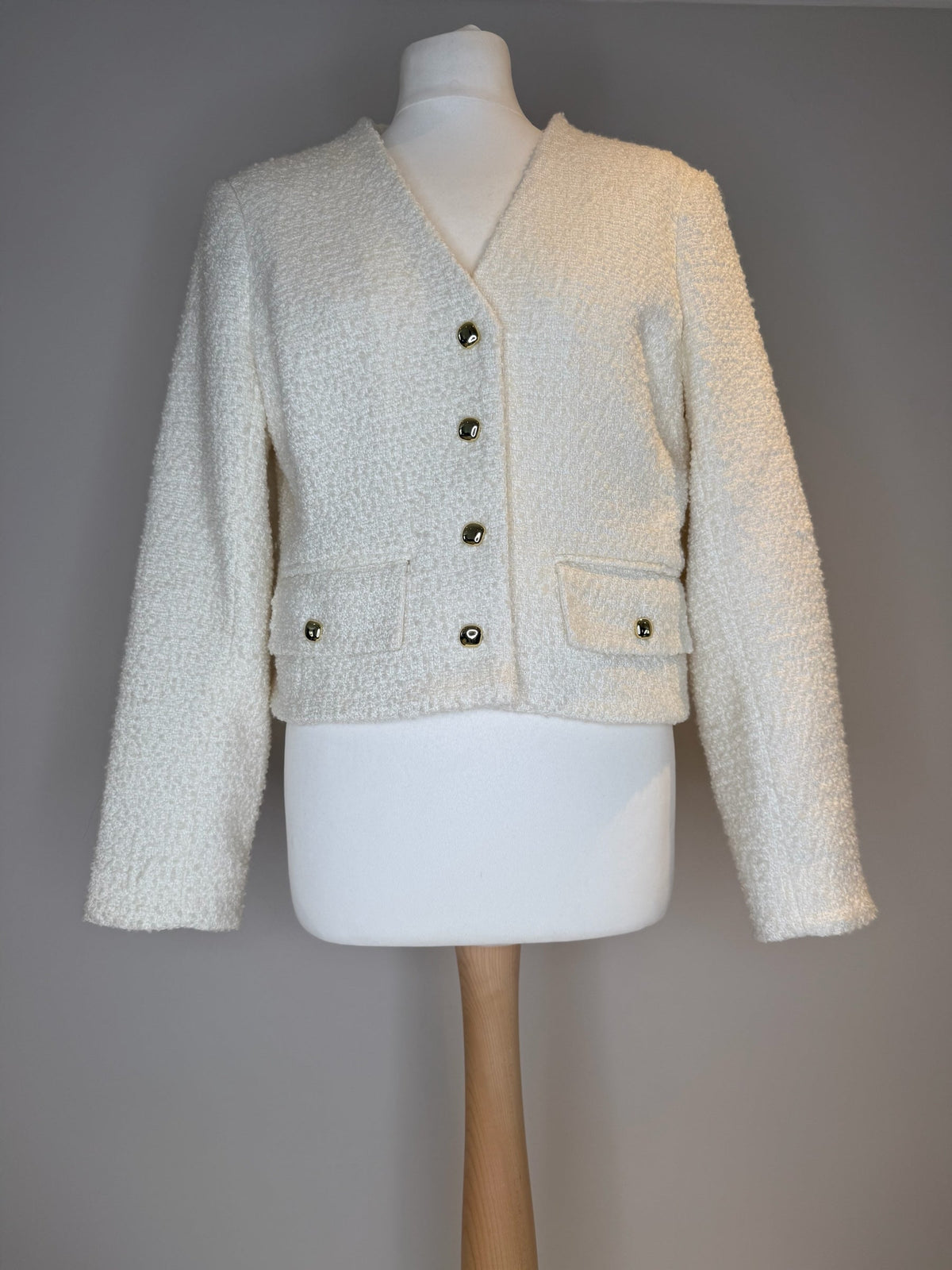 Style Reset cream boucle jacket with a collarless design, gold-tone buttons, and front flap pockets on a mannequin.