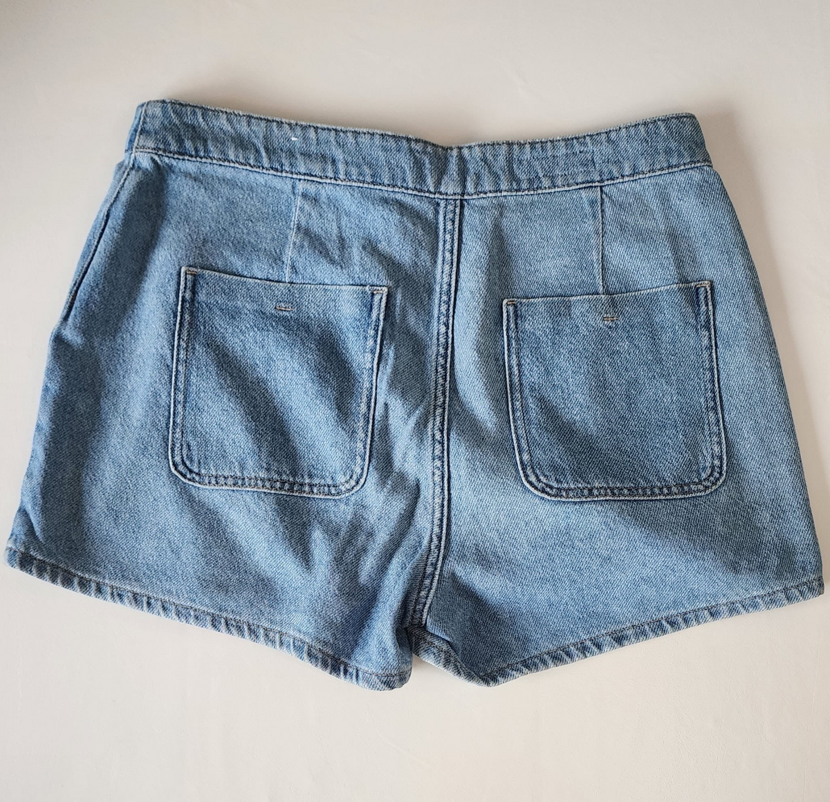 Style Reset light wash denim skort featuring a back view with two functional patch pockets and a mid-rise waistband.