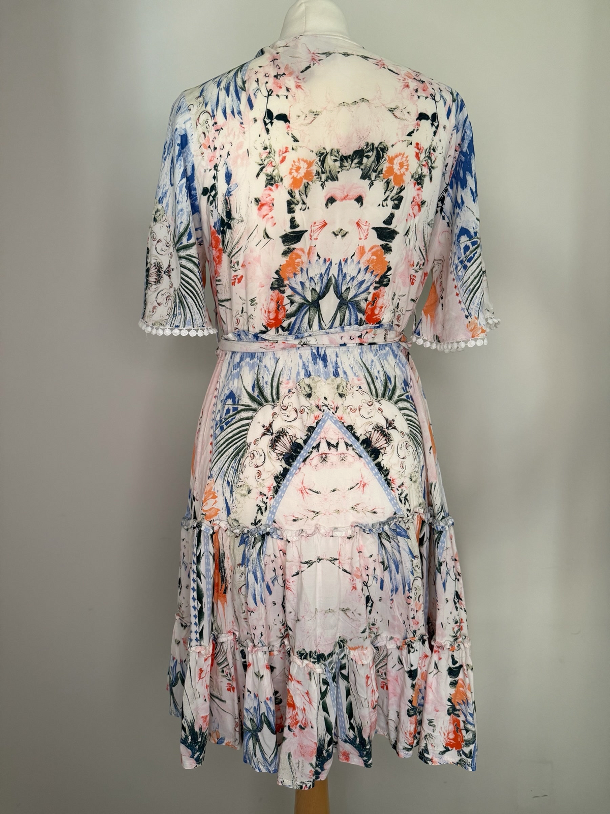 Style Reset JANE midi dress featuring a pastel botanical print, tiered skirt, and pom-pom sleeve trim, back view