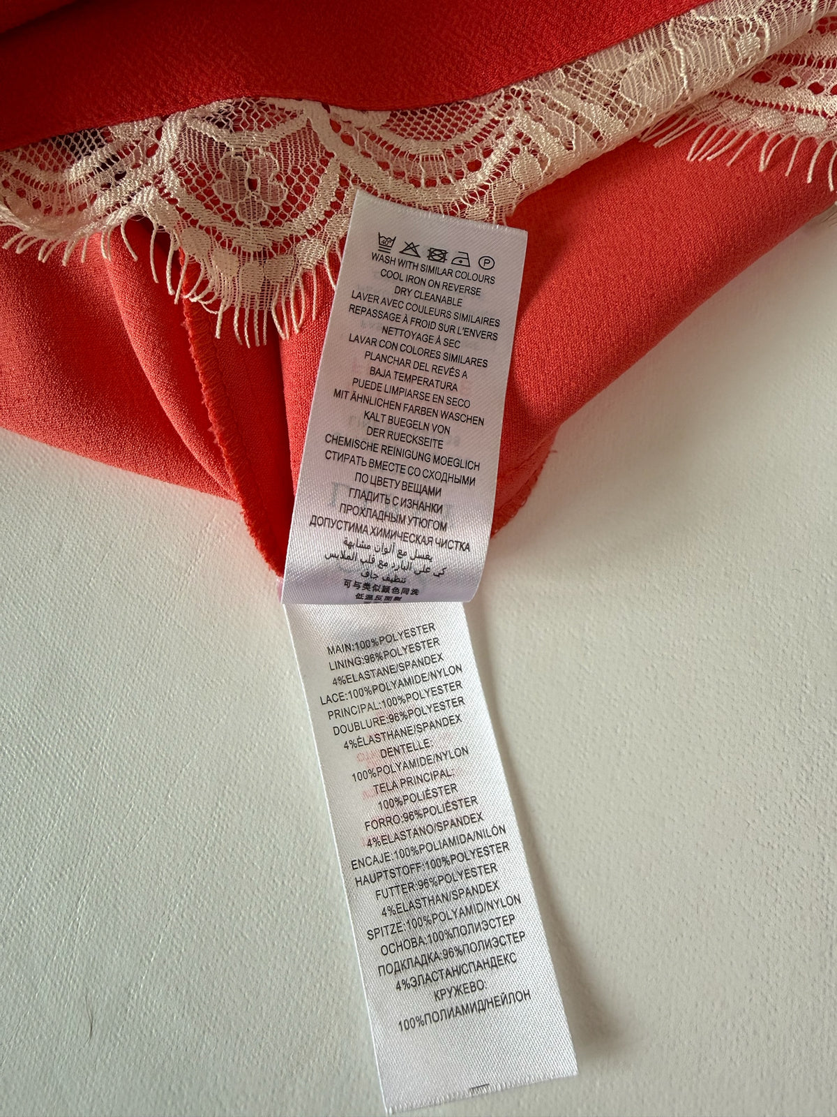 Style Reset Lipsy London dress care label showing coral fabric and cream lace trim with polyester and elastane blend