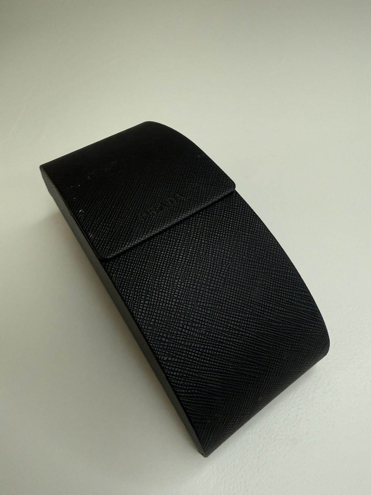 Style Reset black Saffiano-textured Prada sunglasses case with a secure flap closure and embossed logo detail.