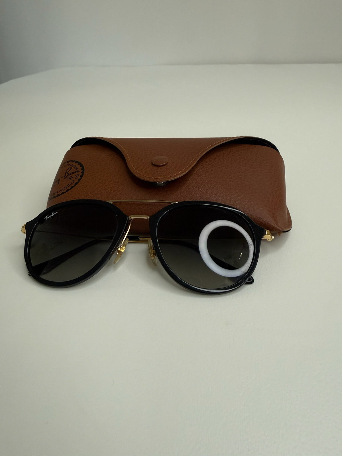 Style Reset Ray-Ban sunglasses with black frames, gold accents, and a tan leather-look protective case on a white table