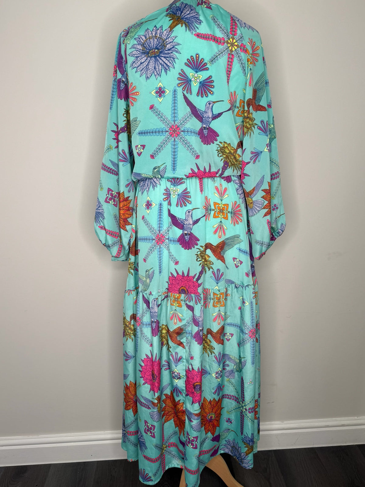 Style Reset turquoise maxi dress with long sleeves, featuring a vibrant hummingbird and floral print, back view.