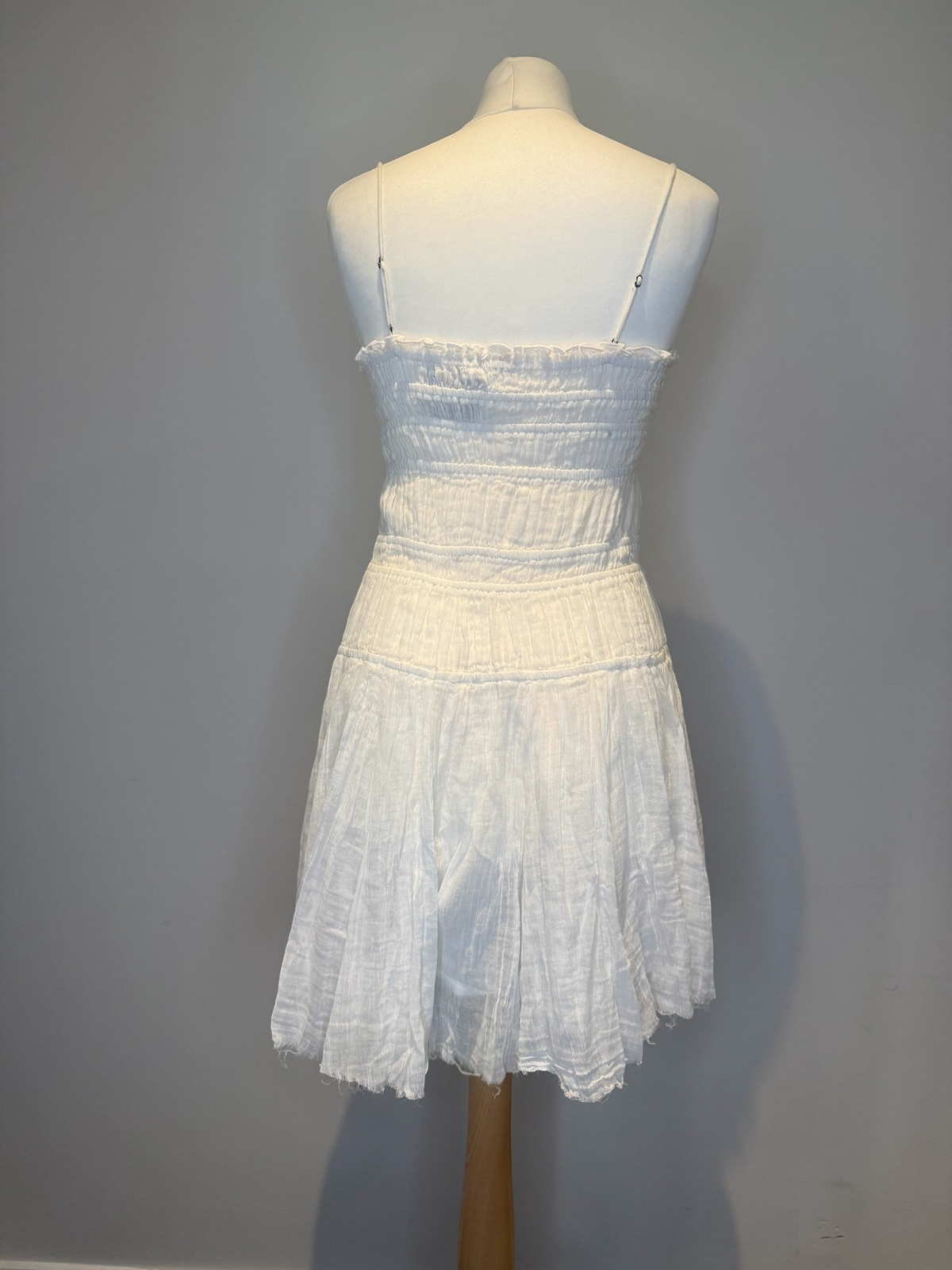 Style Reset white cotton mini dress with a shirred bodice, spaghetti straps, and a raw-edge hem on a mannequin